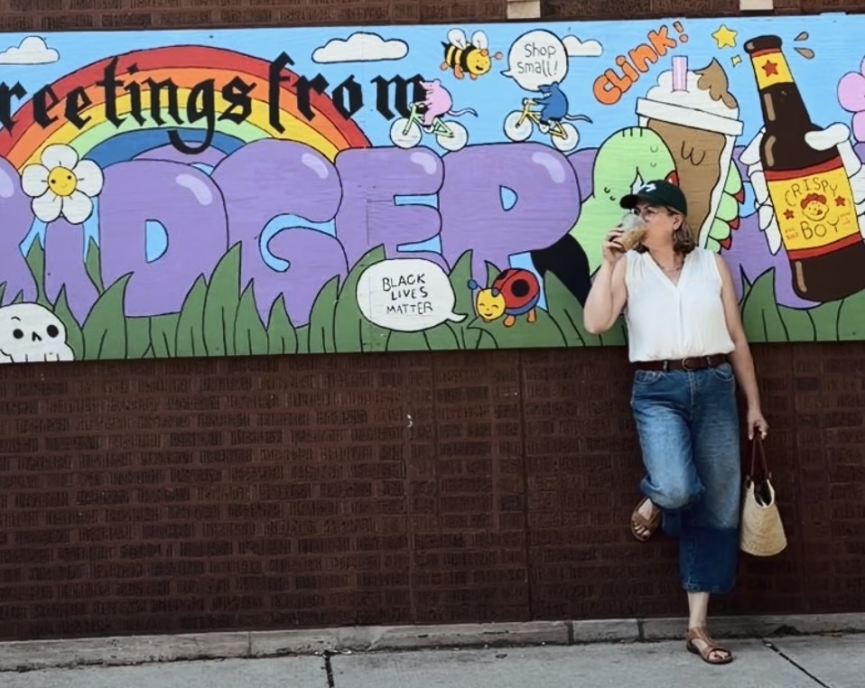 Becky in front of the Greetings from Bridgeport mural in Chicago, holding an iced coffee